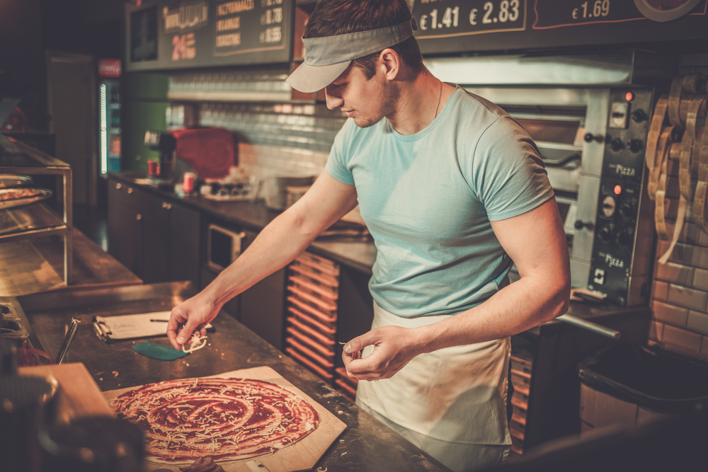 Handsome pizzaiolo making pizza at kitchen in pizzeria